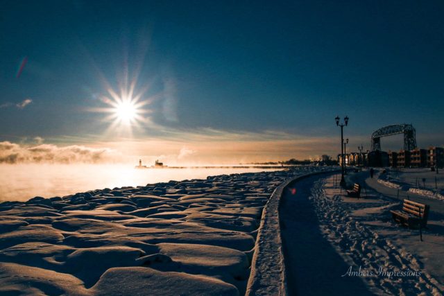 Snowy rocks with water, lift bridge and light house in the distance at sunrise